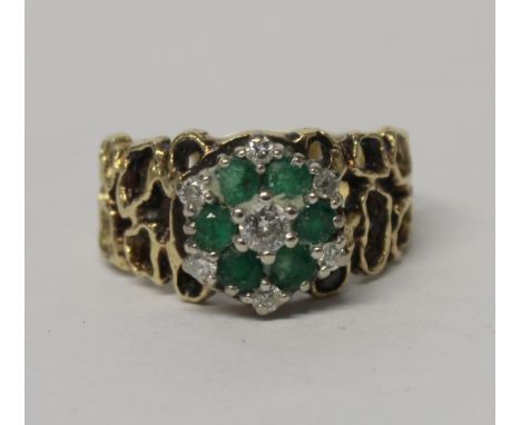 An 18ct yellow gold floral cluster diamond and emerald dress ring with abstract circular filigree shoulders, London 1970, siz