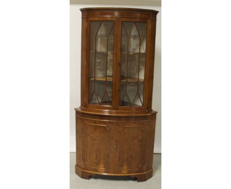 A reproduction walnut floorstanding bow-front corner unit with twin glazed doors above two panelled doors to plinth support, 