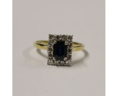 An 18ct yellow gold ladies' dress ring with central emerald-cut blue/green stone (tests as topaz) and diamond surround, size 