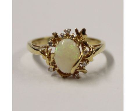 An 18ct yellow gold ladies' dress ring set with central oval cabochon opal, with a scrolling foliate mount set with small whi