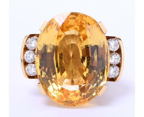 18 kt. Gouden ring, bezet met een ovale helder gele saffier van ca. 42.80 ct. met aan weerszijde drie briljant geslepen diama