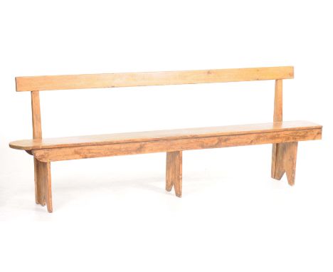 A rustic stained pine benchWith a plain back rail supported on two tapering uprights above a board seat raised on three V cut