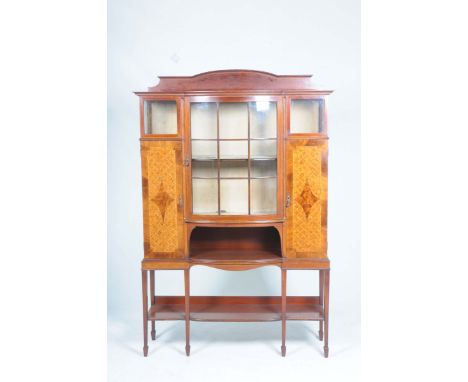 An Edwardian inlaid mahogany display cabinet With an arched pediment above a bowfront glazed and panelled door enclosing a si