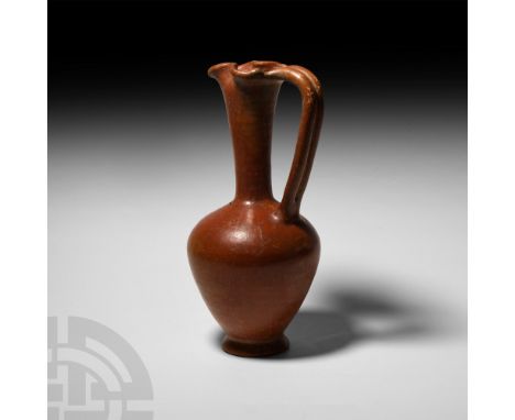 8th century B.C. A piriform ceramic jug with trefoil mouth and integral ribbed handle; covered in a red slip with burnished s