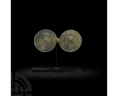 Circa 9th century B.C. A fibula formed from a single filament rolled into two 'spectacle' discs; one of the spirals terminate