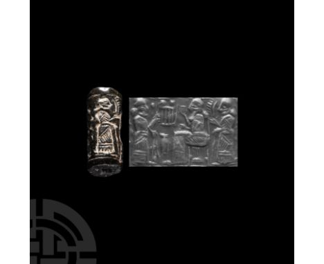 21st century B.C. A dark green jasper cylinder seal with a seated figure of crowned ruler in a flounced robe with a cup in hi