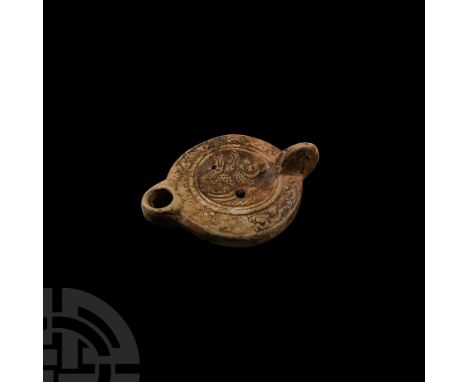 3rd-4th century A.D. A ceramic oil lamp with broad body and short nozzle, lug handle to the rear; decorated with low-relief f