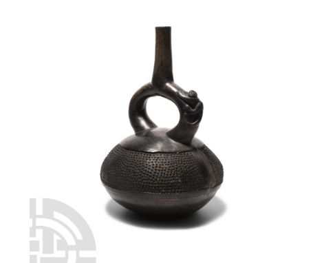 9th-15th century A.D. A blackware stirrup vessel with a squat, carinated body and monkey to one arm of the neck, the upper bo