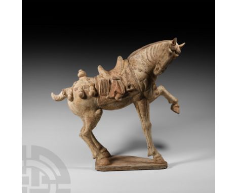 Tang Dynasty, 618-907 A.D. A ceramic caparisoned horse modelled in the round in a prancing posture, on an integral polygonal 