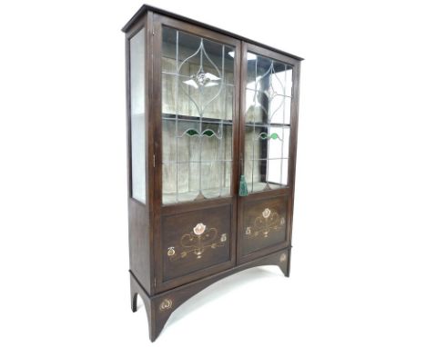 An Art Nouveau mahogany, fruitwood and metal inlaid display cabinet, twin leaded stained glass doors enclosing a single shelf