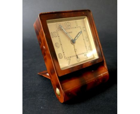 An Art Deco Jaeger LeCoultre travelling alarm clock, in painted metal faux tortoiseshell and brass case with flip front, manu