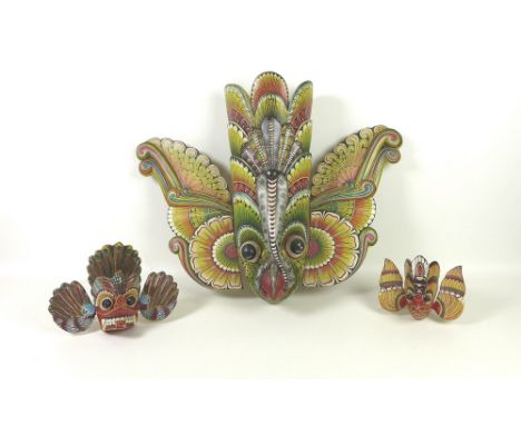 A vintage Sri Lankan hand painted Raksha mask, circa 1960, 47.5cm high, together with two further similar smaller masks. (3)P