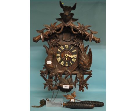 A Black Forest style cuckoo clock, the 13.5 cm diameter dial with Roman numerals, in a wooden case carved dead game, a stags 