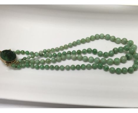 A 1920s jade twin row bead necklace with gold clasp and carved circular panel
