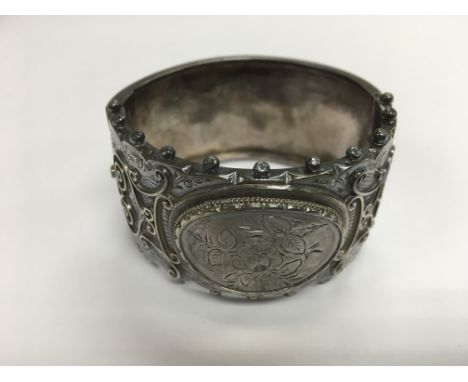 A silver bangle with floral decoration.