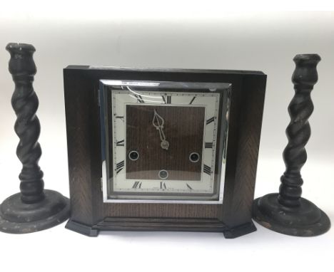 An oak cased mantel clock with a square silvered dial and Roman numerals together with a a pair of barley twist candle sticks