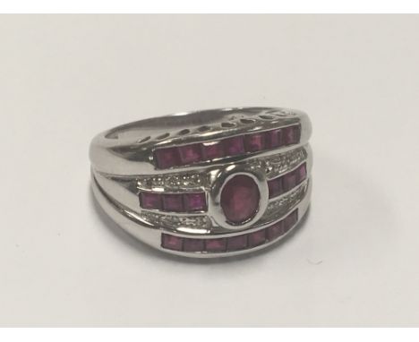 An 18carat white gold ring set with one central ruby with three rows of Ruby’s.ring size O-P.