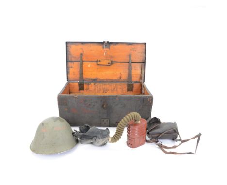 Two gas masks, together with a green tin helmet, cased within a wooden box with hinged lid 