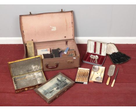 A vintage suitcase with a few pieces of boxed cutlery and empty vintage cutlery boxes.  