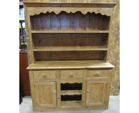 A reclaimed stripped pine kitchen dresser the base enclosed by an arrangement of cupboards and doors with central open shelf,