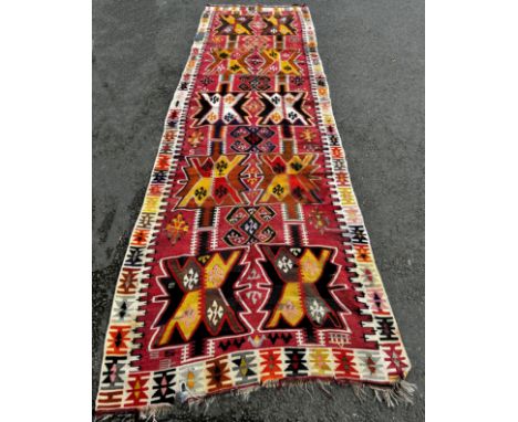 A Kilim Carpet, with bright repeating pattern of X’s on a black field interspersed with geometric stars, 400cm x 120cm approx