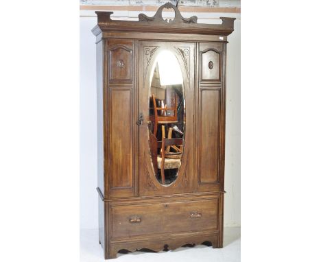 An Edwardian mahogany arts &amp; crafts single wardrobe armoire. Raised on a plinth drawer base with oval mirror door centre 