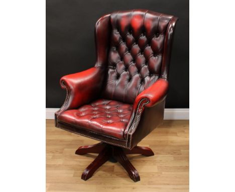 A Chesterfield style wingback swivel armchair, deep-button upholstery, scroll arms, 116cm high, 83cm wide, the seat 44cm wide