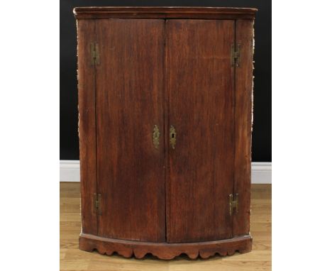 A 19th century oak bow front corner cupboard, moulded cornice above a pair of doors enclosing three shelves, shaped apron, 10