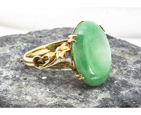 A high carat gold and jade dress ring, the polished oval jade panel within a four claw setting, with scroll floral pierced sh