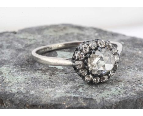 An antique platinum diamond cluster ring, the rose cut central diamond surrounded by a bezel of old cuts set in silver tipped