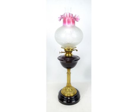 A late Victorian brass oil lamp with dark ruby red glass reservoir, floral decorated shade and spreading circular foot, heigh