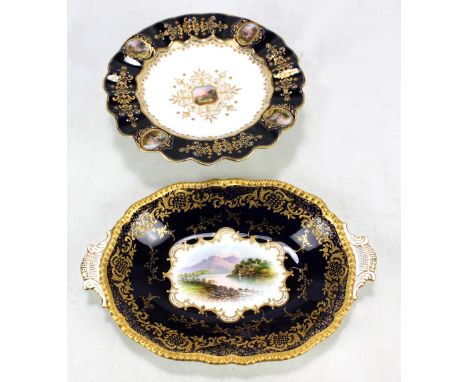 A Coalport 'Jewelled' landscape decorated gilt heightened tazza with scallop moulded dark blue border set with four oval land