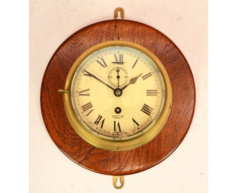 A Smiths Astral brass bulkhead clock, having 8 day movement, mounted on a mahogany backplate, 20cm diameter. 