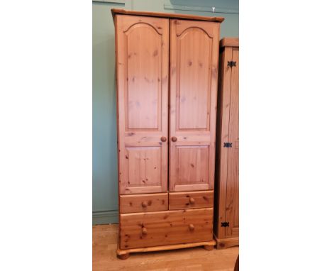 A modern pine tallboy/wardrobe, the twin long doors opening to fitted clothes rail and shelf, over one deep and two short dra