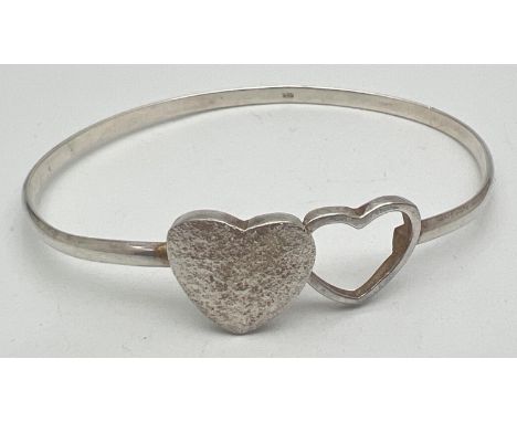 A modern design double heart silver bangle with hook clasp. Central brushed silver and open work hearts. Silver mark to insid