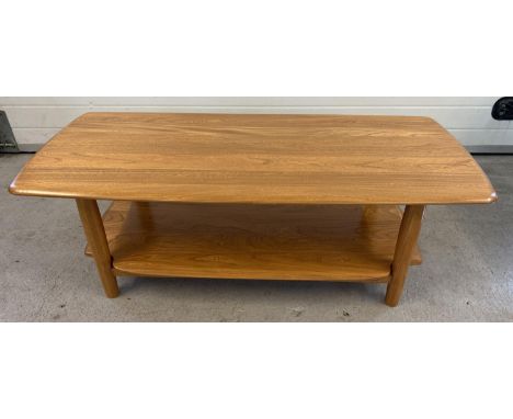 A modern Ercol light wood coffee table with rounded edges, undershelf and cylindrical legs. Approx. 45.5cm tall x 130cm long.