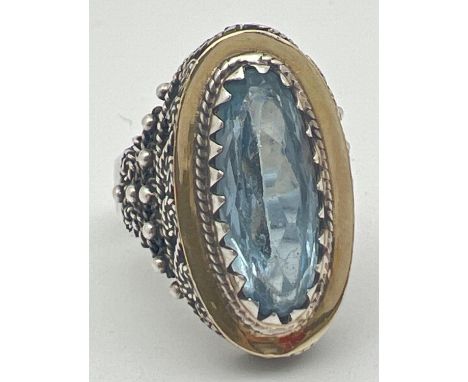 A silver modern design dress ring set with a large oval cut blue topaz stone. Rope design scroll detail to mount and shoulder