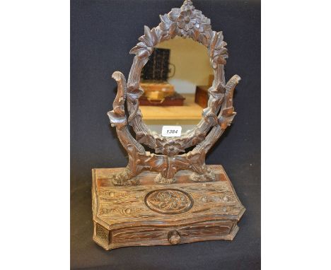 A Black Forest dressing table mirror, oval plate, the canted base with long drawer, carved throughout, with flowers, leafy br