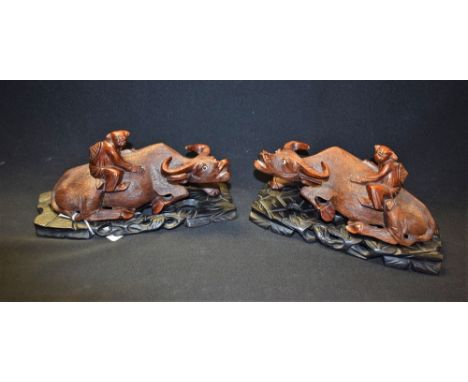 A pair of Chinese hardwood carvings, of boys astride water buffaloes, the beasts with inset glass eyes, ebonised hardwood pie
