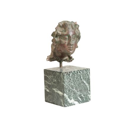 A ROMAN BRONZE MOUNT cast as horned Satyr with animal pelt tied at the neck, probably 1st/2nd Century, on a contemporary marb