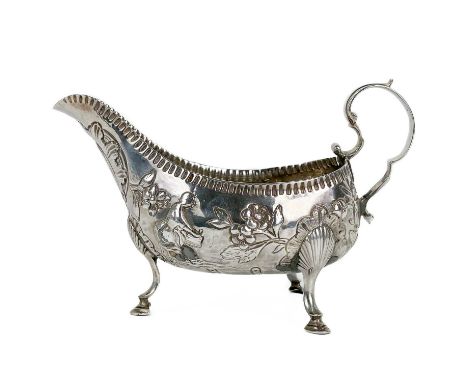 A George III Irish silver gravy boat by Matthew West. With gadrooned rim, a leaf and scroll handle, embossed with milk maids 