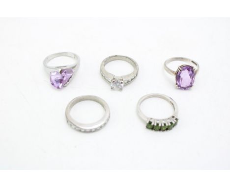 A group of five white metal rings, including a silver and purple stone ring, likely amethyst, another set with purple paste, 