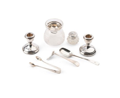 A collection of silver items to include a pair of candlesticks, lidded jar, silver spoon, sugar tongs and other similar items