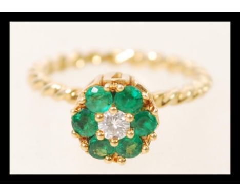 An 18ct gold twist flower head ring set with six brilliant cut emeralds around a central diamond. Size K. Weight 3.6g.