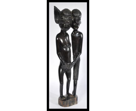 A west African polished wood fertility sculpture depicting two supernatural figures raised on a wooden base having elongated 