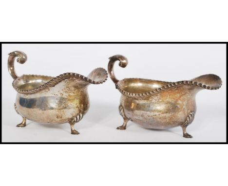 A pair of early 20th century silver hallmarked sauce gravy boats raised on hood feet with acanthus leaf joints. The shaped po