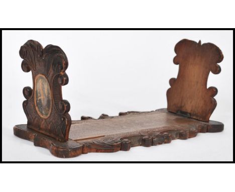 A 19th century Victorian carved wooden Blackforest book trough / slide having scrolled decoration with painted cartouche pane