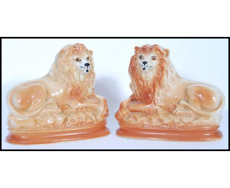 A pair of recumbent Staffordshire ceramic fire dogs in the form of lions having glass eyes and gilt detailing.&nbsp;Measures 