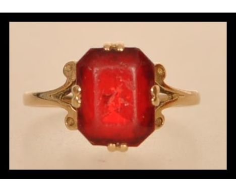 An early 20th century hallmarked 9ct gold ring set with an octagon cut red stone and scrolled shoulders. Hallmarked London. S