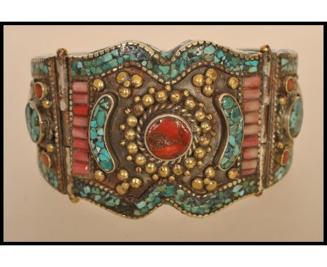 A Chinese / Himalayan silver white metal bangle bracelet set with coral cabochons, turquoise and carnelian stones.